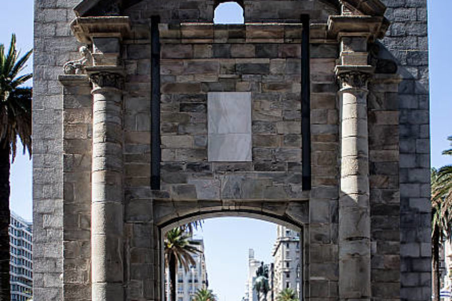 Montevideo, Uruguay - April 11, 2015: A far off group of people walking toward the landmark known as the Gateway of the Citadel (Puerta de la Ciudadela) in Montevideo. Beyond the entryway is Independence Plaza in the Old City Area of Montevideo. It is one of the only remaining structures that were once part of a wall that surrounded the oldest neighborhood in the city. It was built in the 1700s and mostly torn down, with this passageway remaining in 1829.