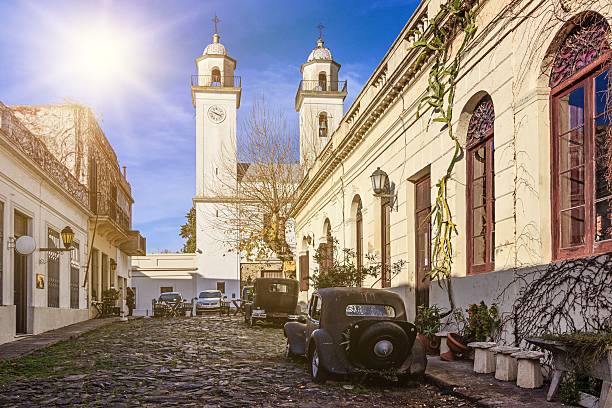 Colonia del Sacramento (formerly the Portuguese Colónia do Sacramento) is a city in southwestern Uruguay, by the Río de la Plata. It is renowned for its historic quarter, a UNESCO World Heritage Site.View towards alley in the historic quarter, with ancient car and the only church in town (Basílica del Santísimo Sacramento). Sun well visible.